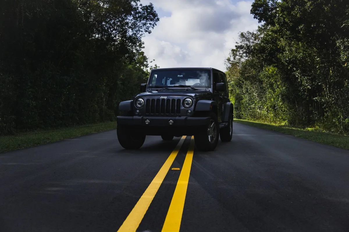 A black Jeep driving on an open road through a lush green forest in summer. A black Jeep driving on an open road through a lush green forest in summer.