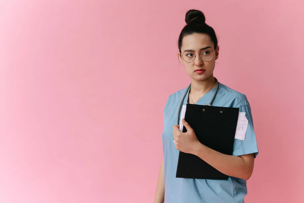 Confident female doctor in scrubs holding a clipboard against a pink background. Confident female doctor in scrubs holding a clipboard against a pink background.