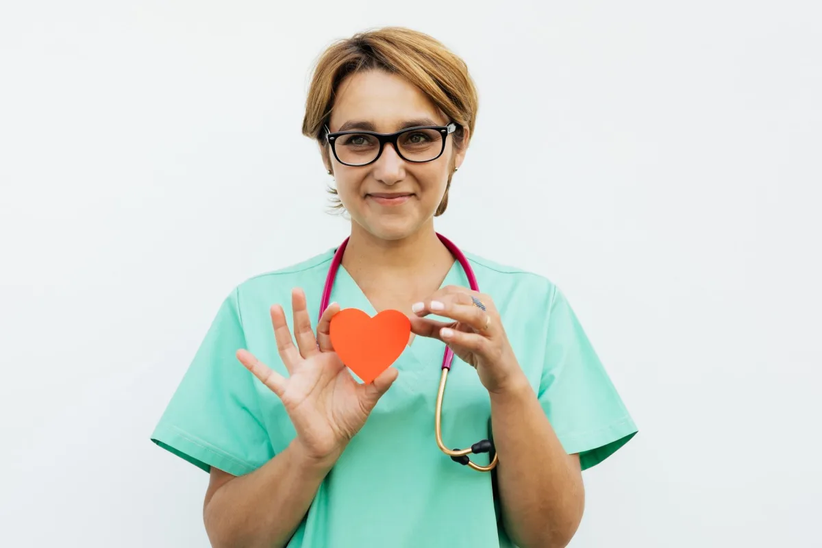 Female doctor in scrubs holding a paper heart symbol, smiling with a stethoscope around her neck. Female doctor in scrubs holding a paper heart symbol, smiling with a stethoscope around her neck.