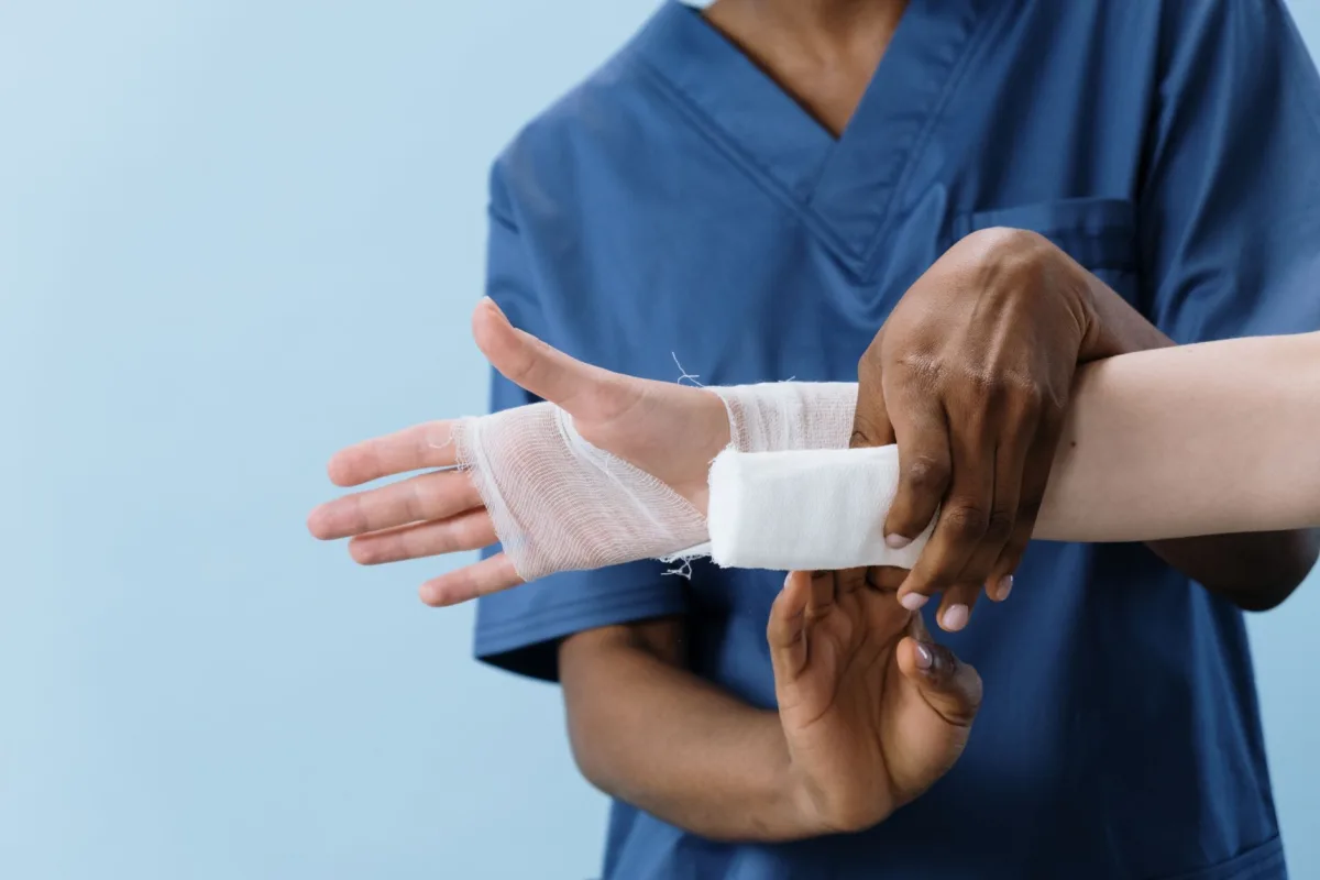 A medical professional carefully wrapping a bandage around an injured person's hand. A medical professional carefully wrapping a bandage around an injured person's hand.