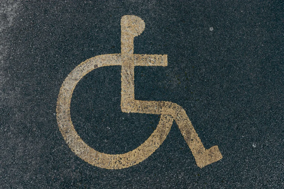 Close-up of a yellow accessibility symbol marked on a dark asphalt surface. Close-up of a yellow accessibility symbol marked on a dark asphalt surface.