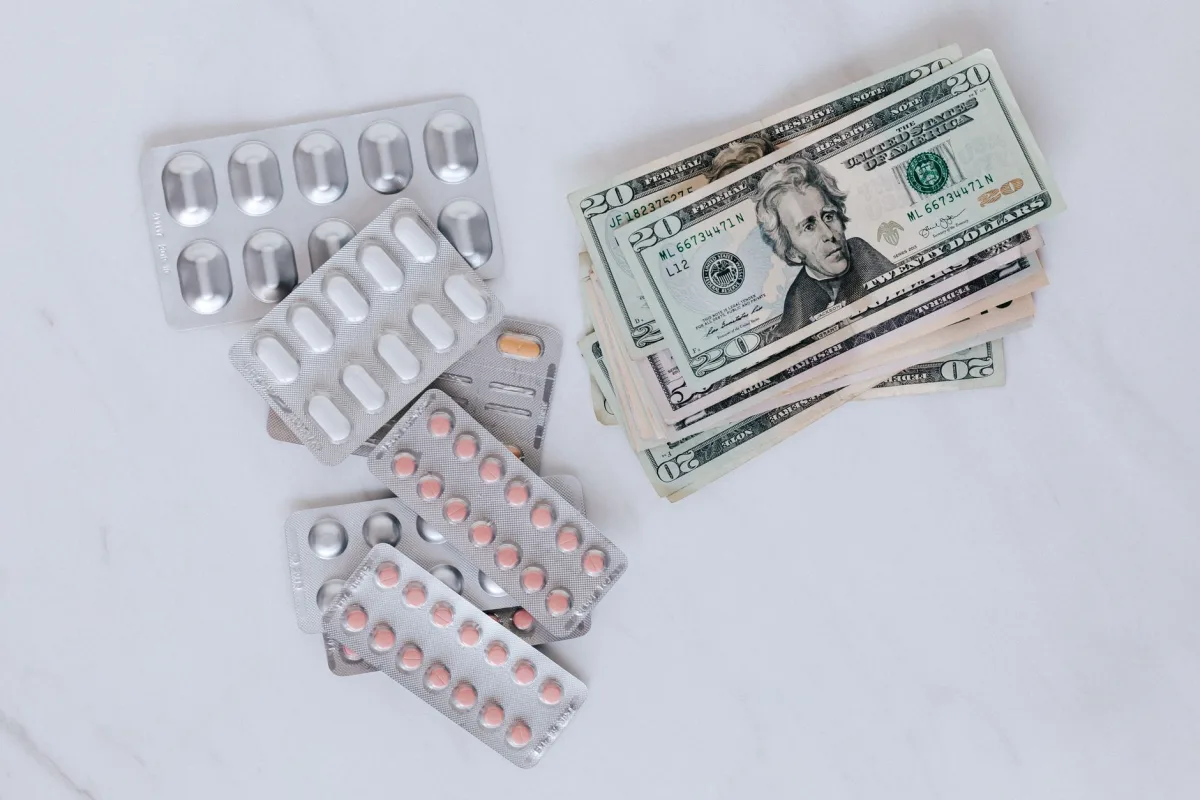From above of silver blister full of drug near big pile of dollar to spend on medication From above of silver blister full of drug near big pile of dollar to spend on medication
