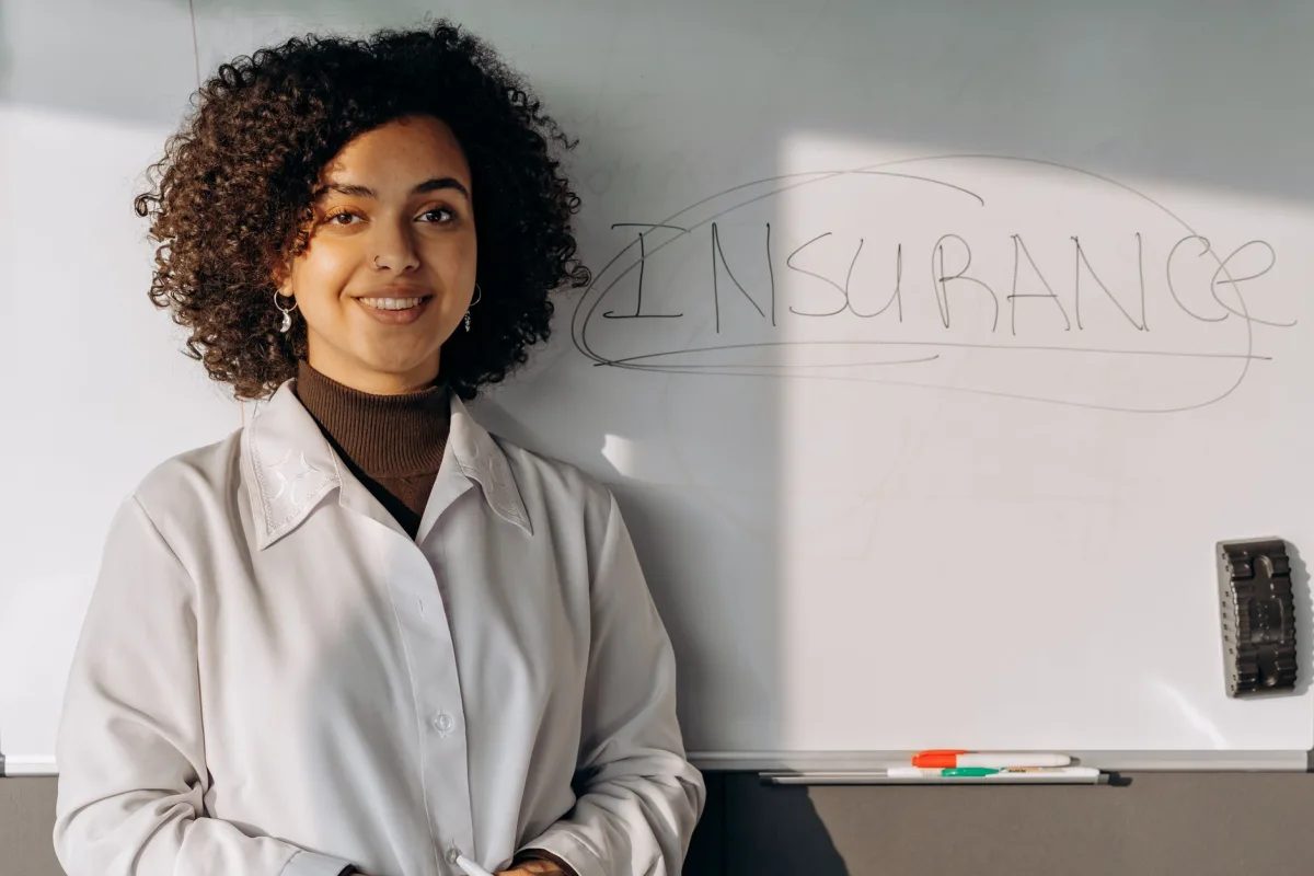 African American woman smiling in office setting with whiteboard displaying 'Insurance'.