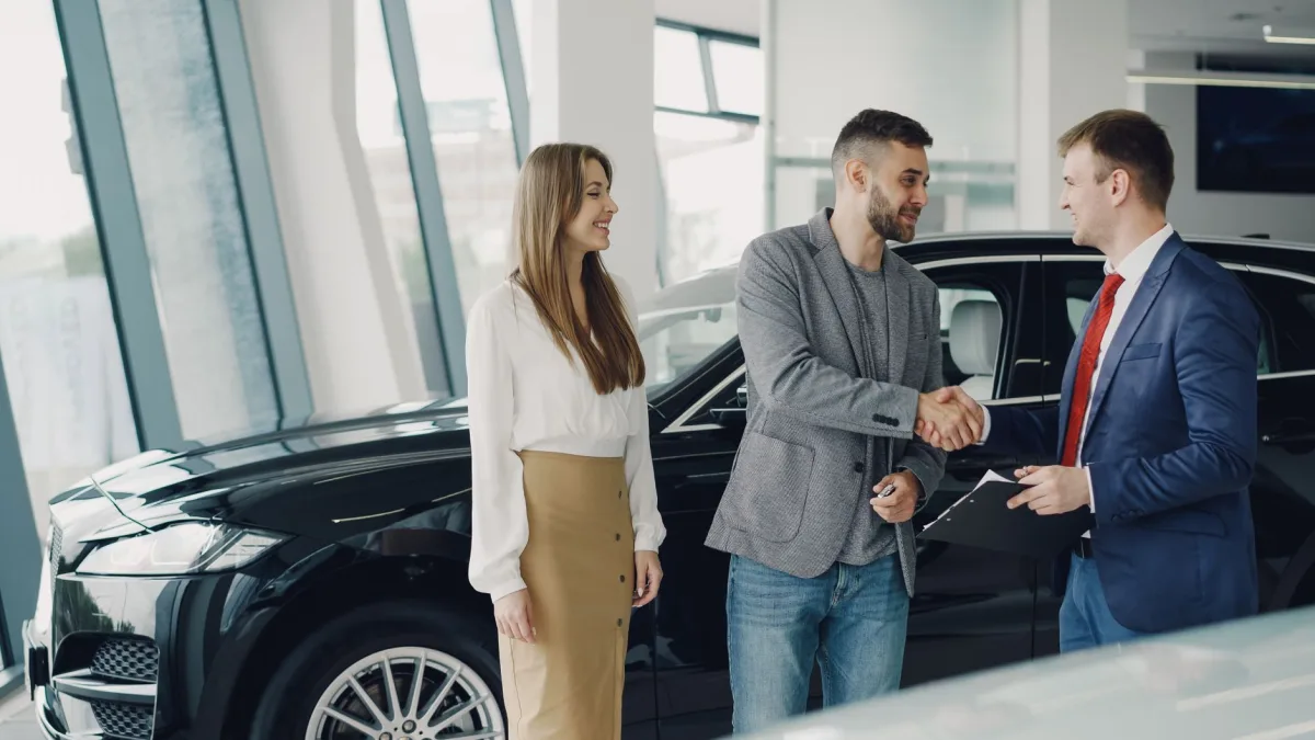 Customers shaking hands with dealer in showroom, sealing car purchase deal.