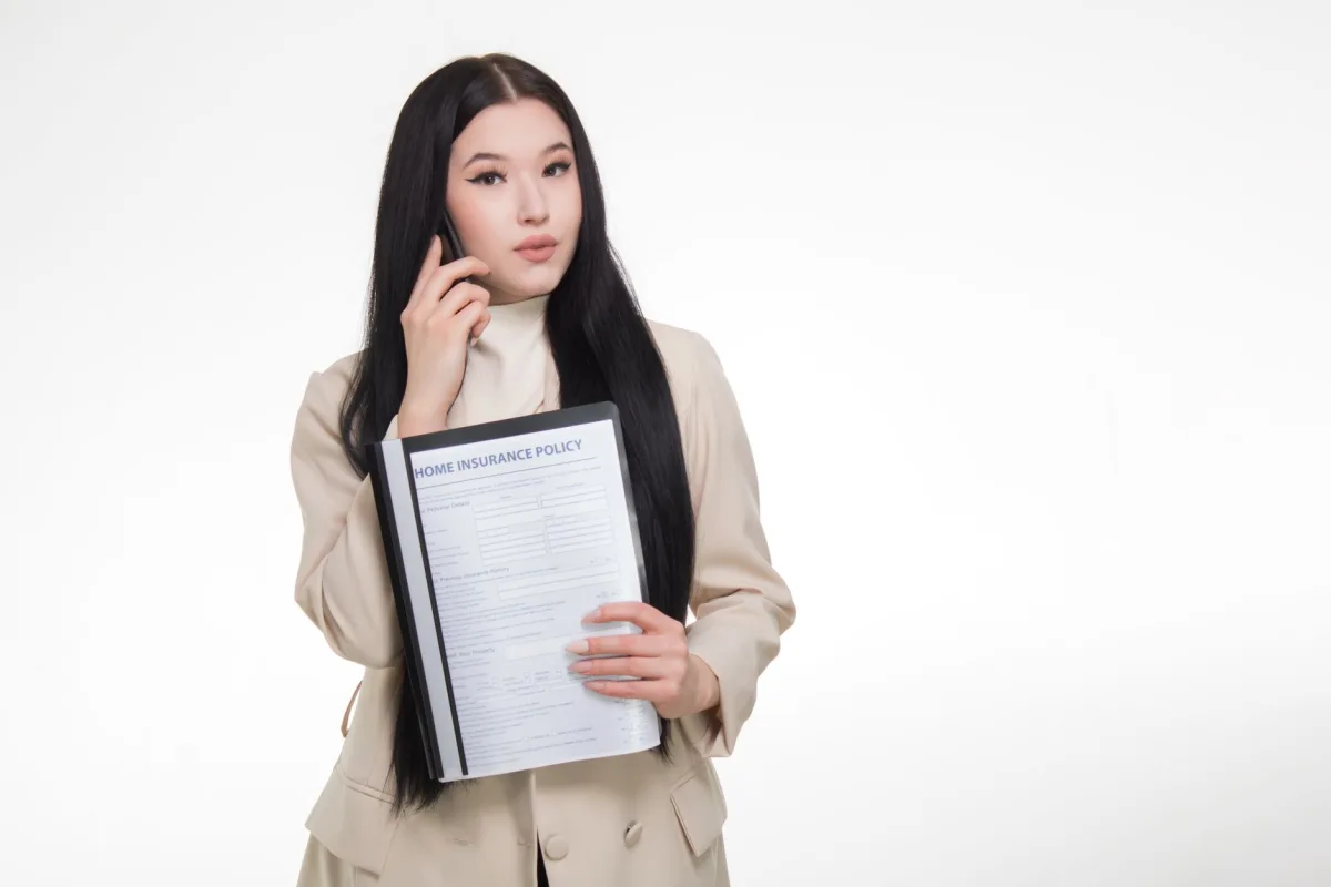 Asian woman in business attire holding home policy while on a phone