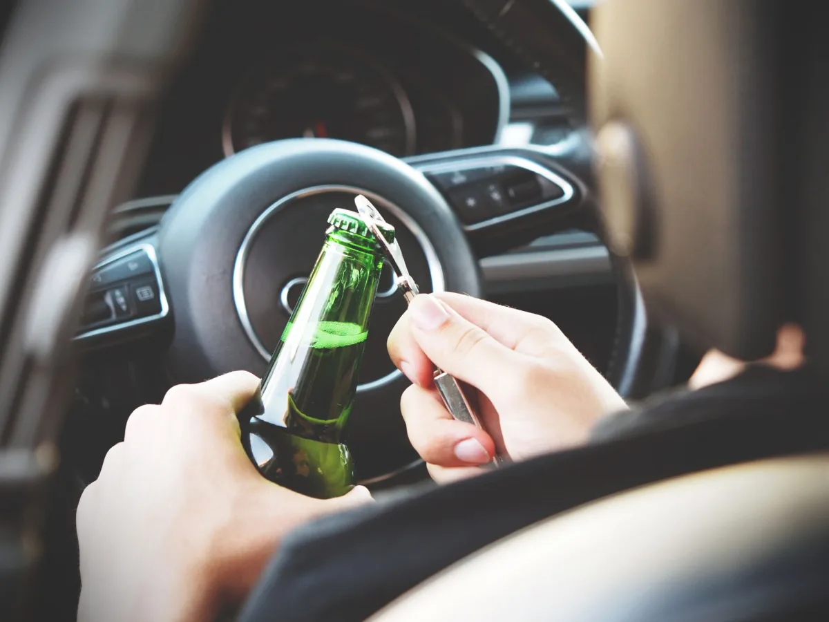 Hands opening a beer bottle inside a car, highlighting the importance of safe driving and awareness of road dangers. Hands opening a beer bottle inside a car, highlighting the importance of safe driving and awareness of road dangers.