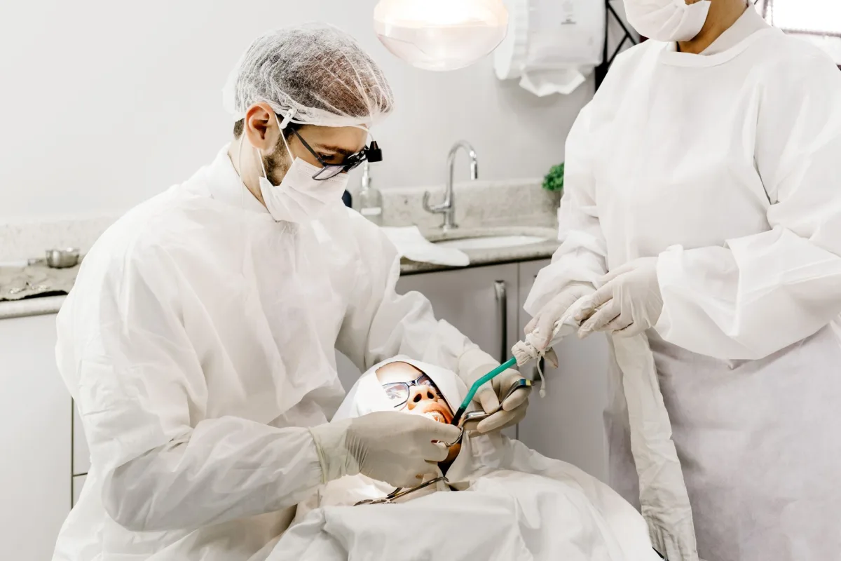 From above of unrecognizable male stomatologist and female assistant in uniforms treating patient teeth in clinic From above of unrecognizable male stomatologist and female assistant in uniforms treating patient teeth in clinic