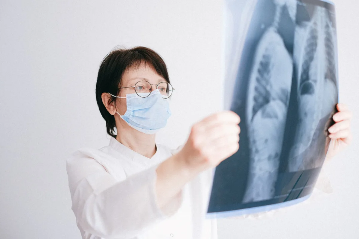 Doctor analyzes x-ray wearing a mask in a clinical setting.