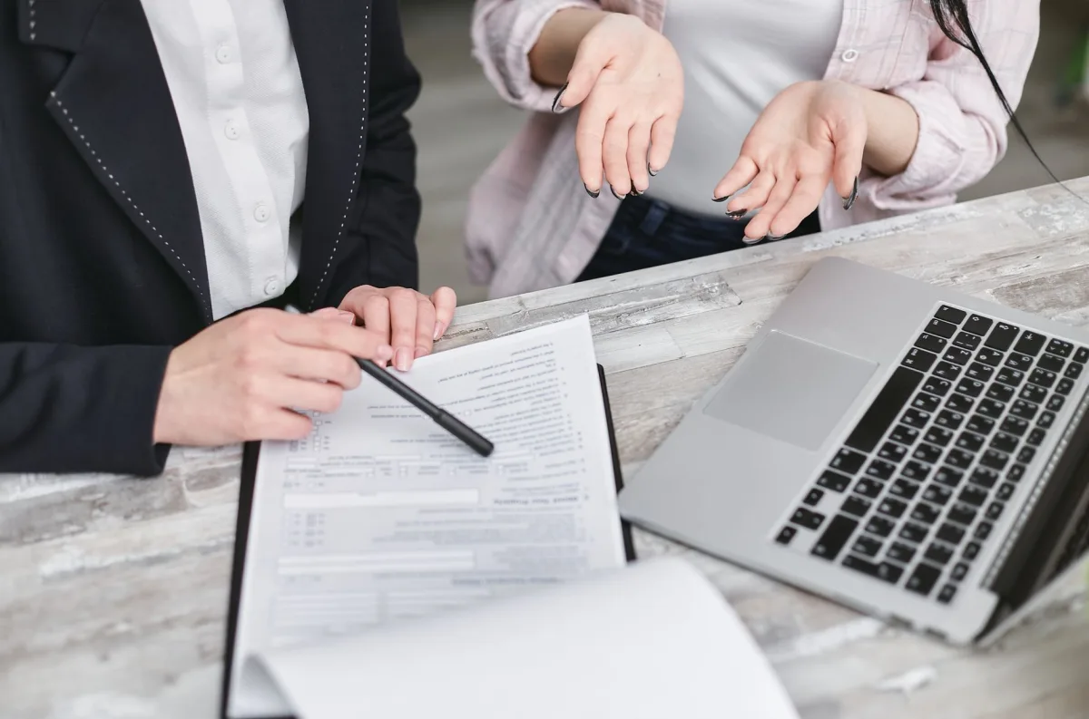 Two professionals discussing contract at business meeting with documents and laptop. Two professionals discussing contract at business meeting with documents and laptop.