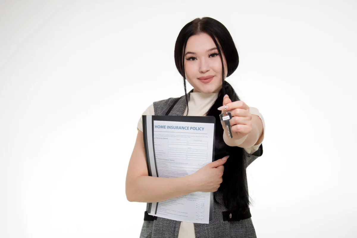 Asian woman smiling while holding a home policy and a key, symbolizing new home ownership. Asian woman smiling while holding a home policy and a key, symbolizing new home ownership.