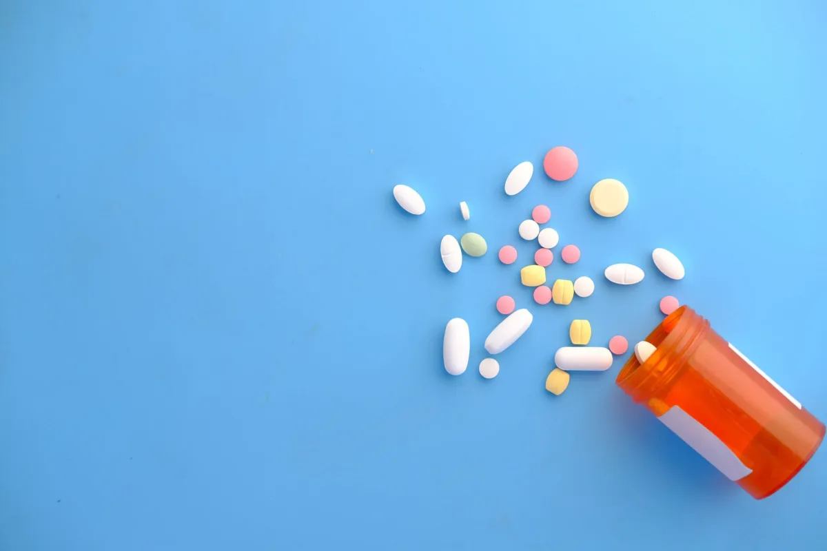 An assortment of colorful pills scattered from a prescription bottle on a blue background.