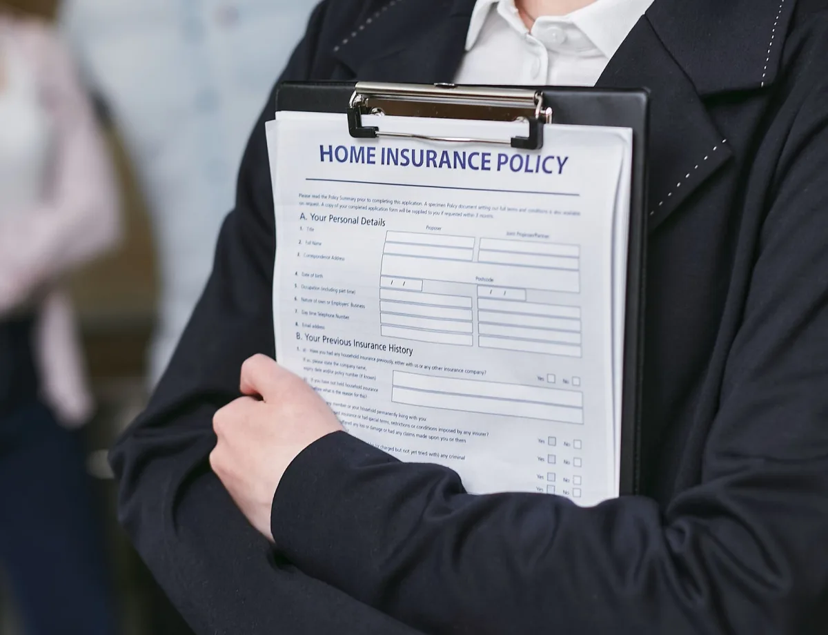 Close-up of a person holding a home policy on a clipboard, captured indoors.