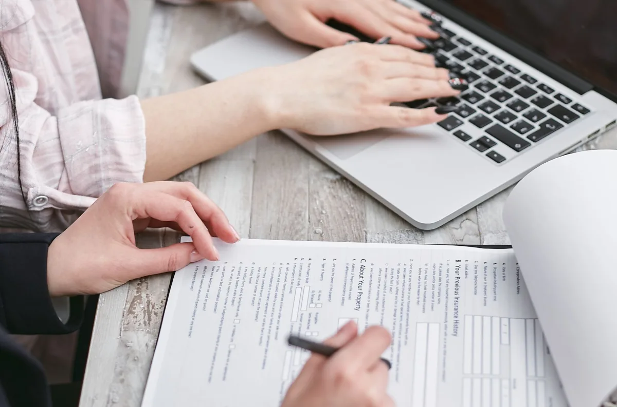 Close-up of hands typing on a laptop and reviewing business documents, focused on finance and legal tasks. Close-up of hands typing on a laptop and reviewing business documents, focused on finance and legal tasks.