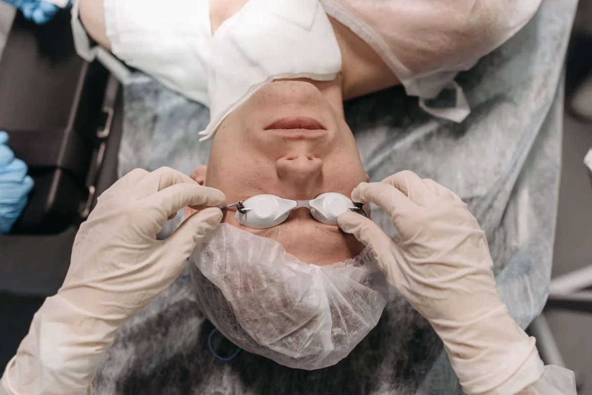 Patient lies on surgical table as medical professional adjusts protective eyewear.