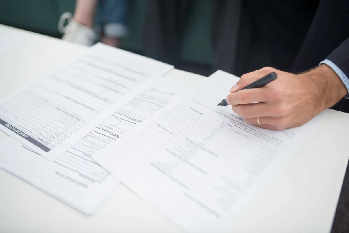 Close-up of a hand signing documents in an office setting.